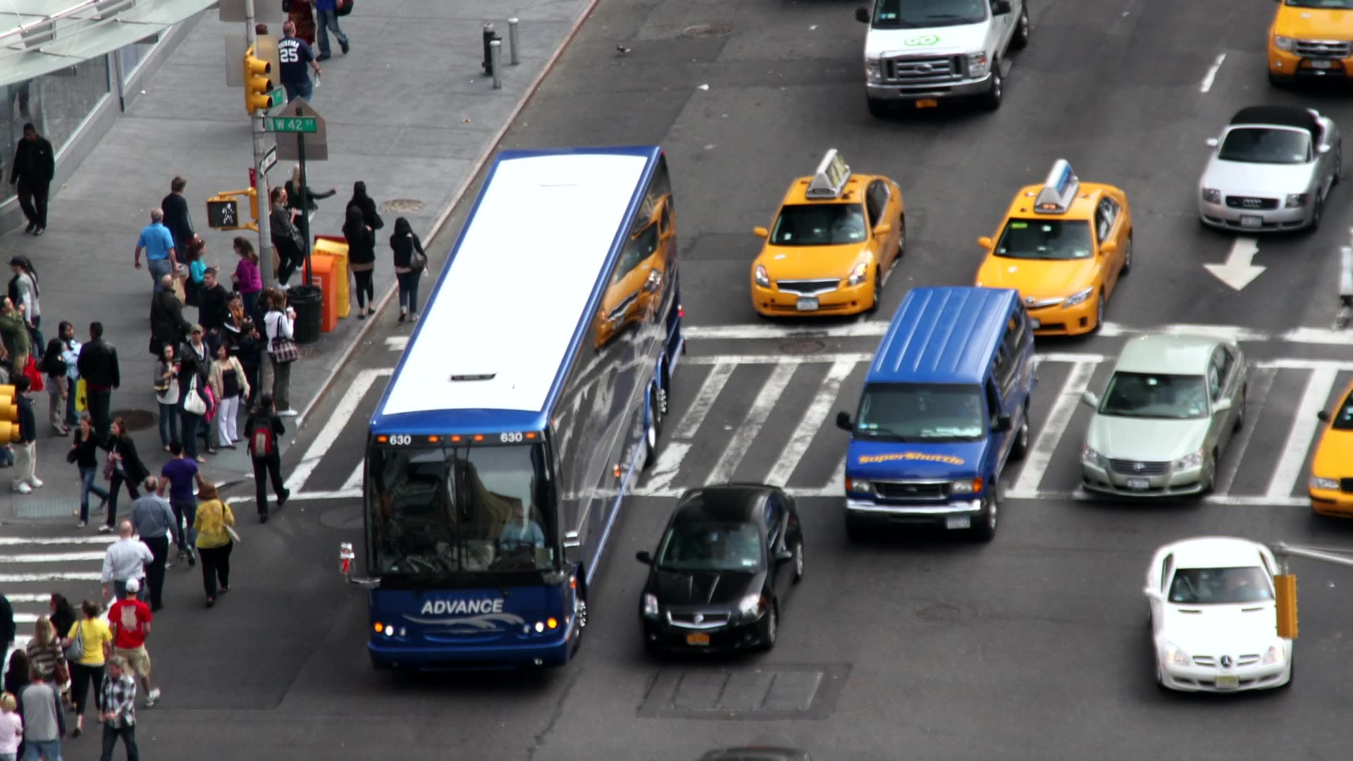 Busy city intersection with taxis, a bus, and pedestrians seen from above
